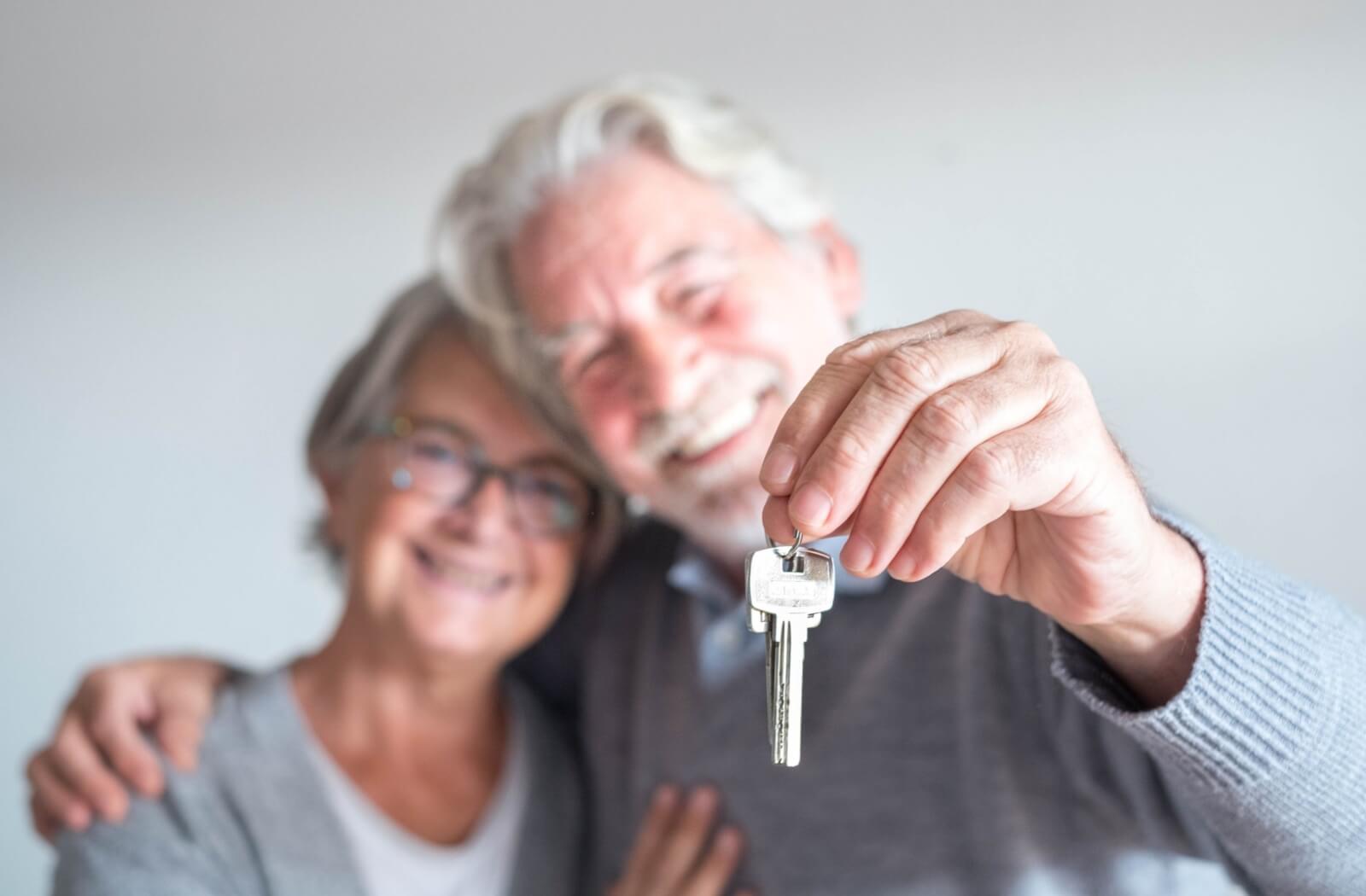 Two older adults smile and hold up the key to their new home in independent living