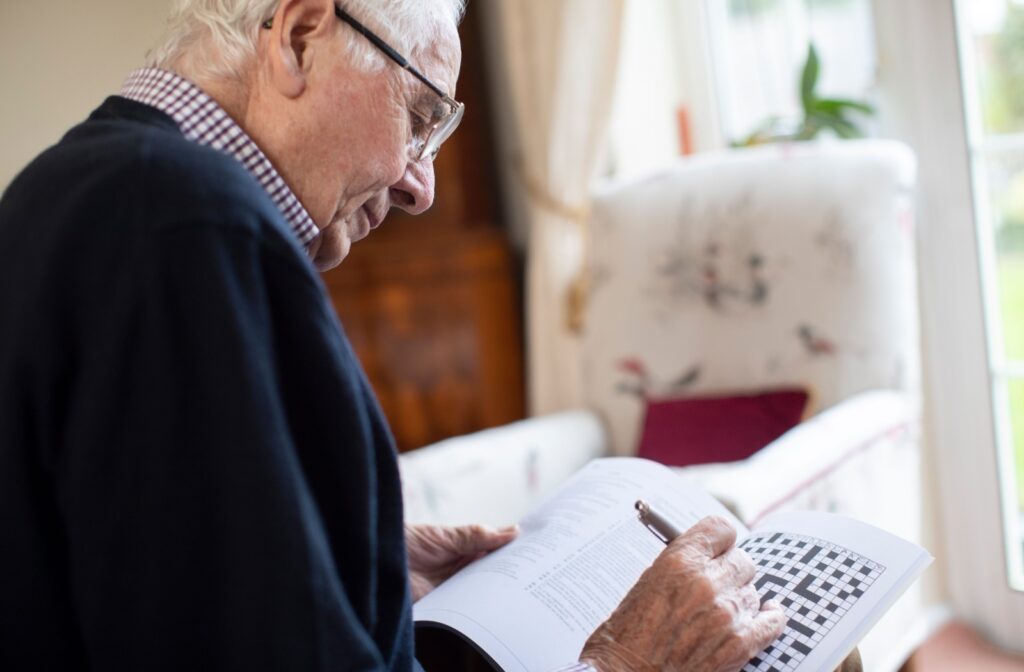 A senior is sitting in a brightly lit room, working on some crossword puzzles.