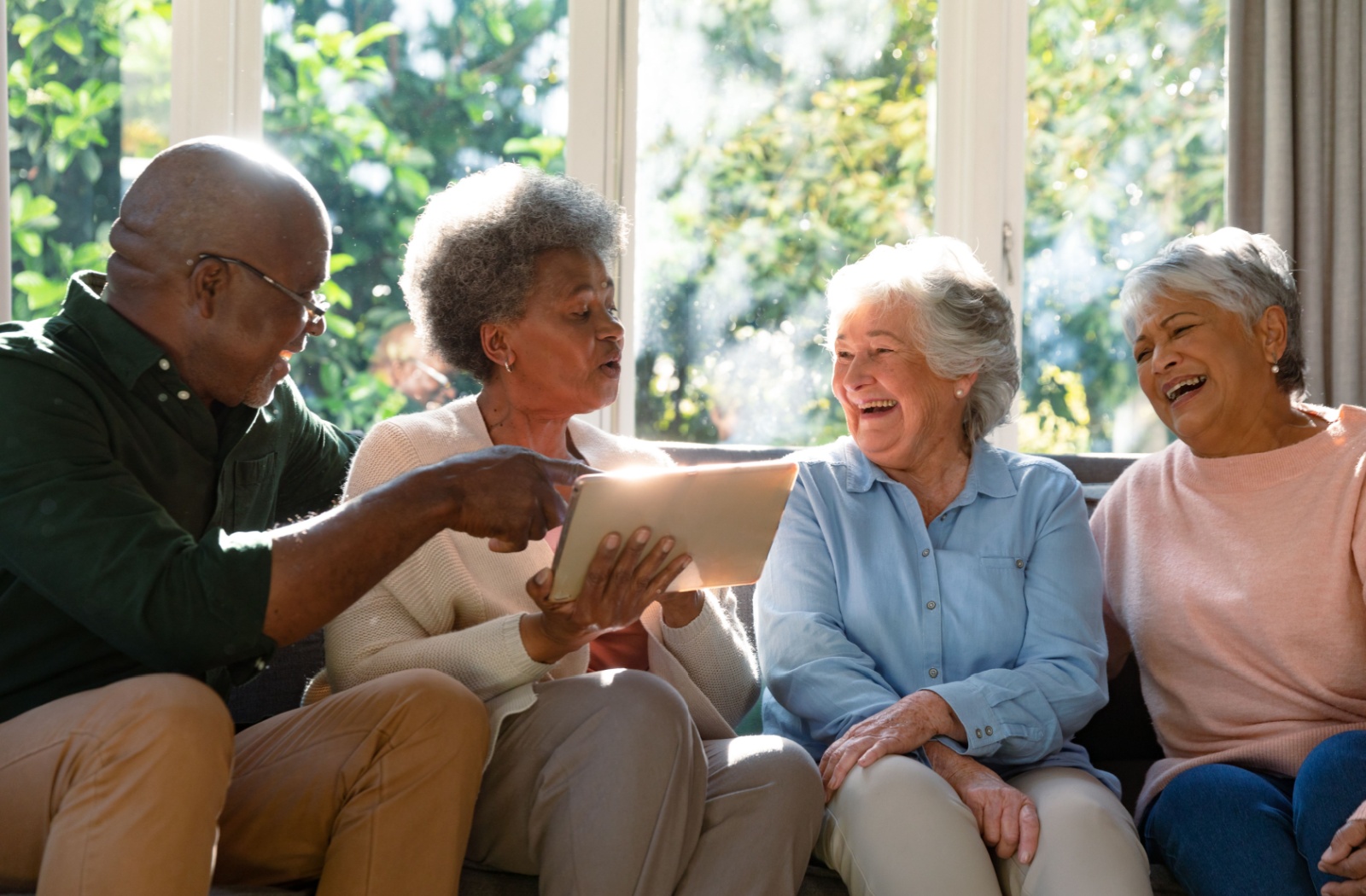 A group of seniors laugh as they play a game on a tablet computer together.