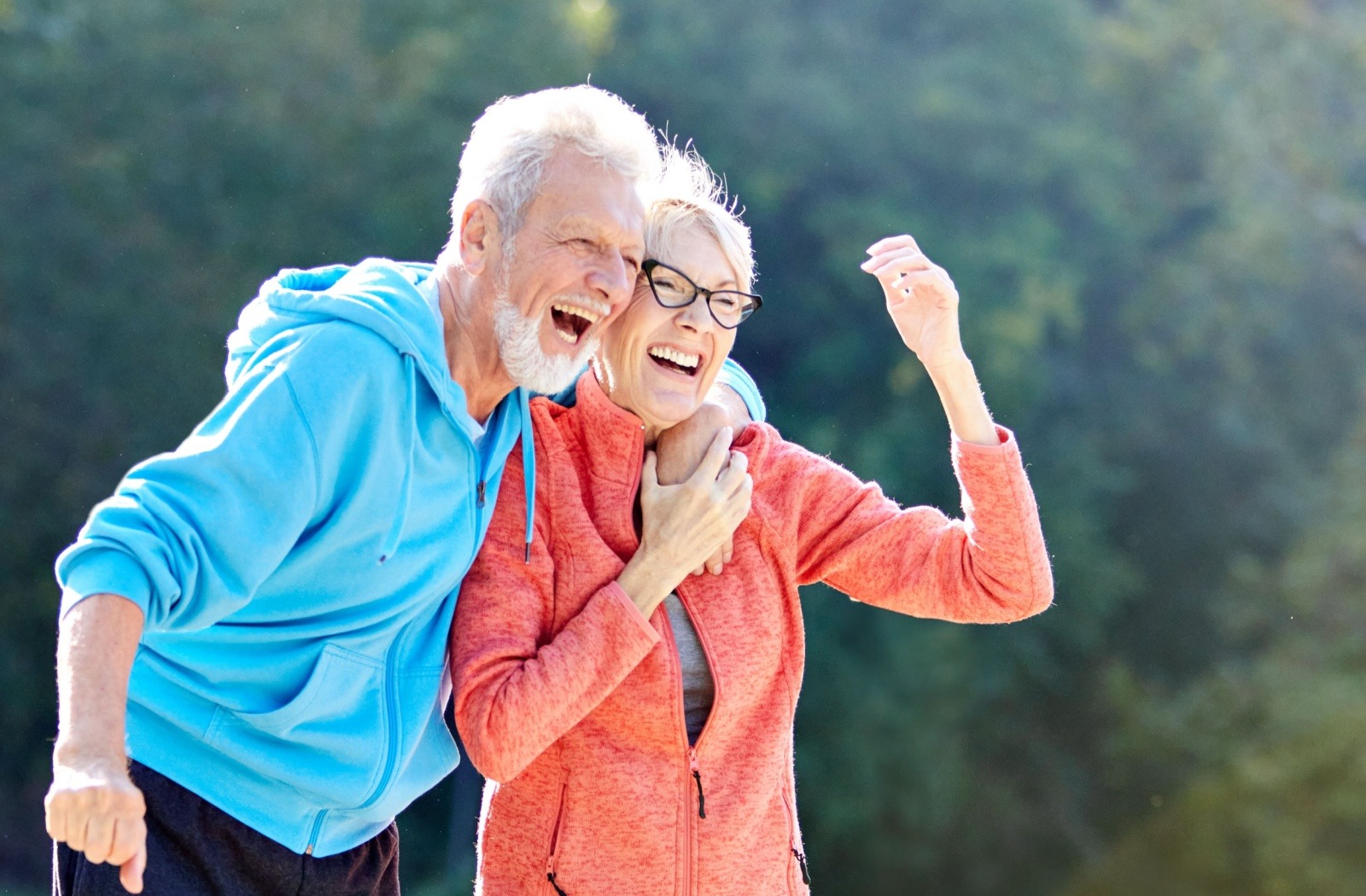 A senior couple laugh as they enjoy a brisk outdoor walk together.