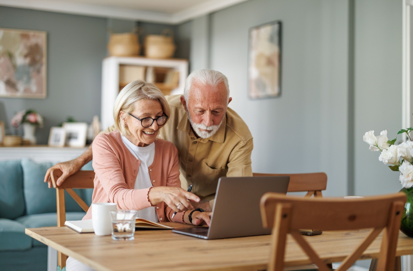 A senior couple research independent living options together on a laptop at their dining room table.